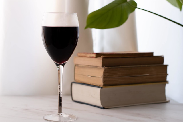 Glass of red wine on a table with a stack of books.